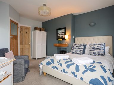 A bedroom with a bed with blue and white bedding a chair a white wardrobe and wooden doors at Min Y Mor Trearddur Bay in Trearddur Bay