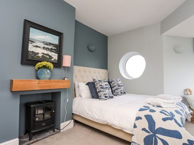 A bedroom with a bed a painting on the wall a small stove and a round window at Min Y Mor Trearddur Bay