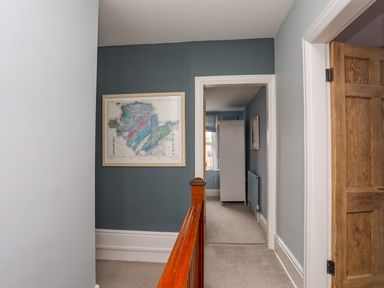 A hallway with gray walls, beige carpet, a wooden banister, a framed map, and an open door at Min Y Mor Trearddur Bay