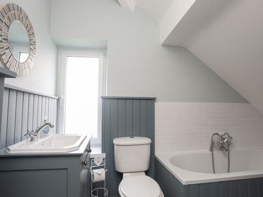 A bathroom with a toilet sink bathtub and round mirror at Min Y Mor Trearddur Bay