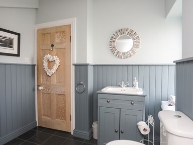 A bathroom with a wooden door with a heart-shaped decoration a sink with a mirror above and a toilet at Min Y Mor Trearddur Bay
