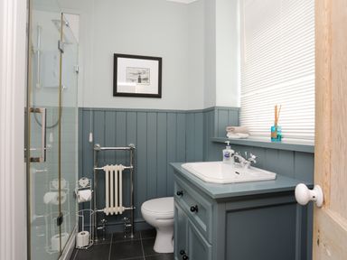 A bathroom with a shower, toilet, sink, towel, and framed picture at Min Y Mor Trearddur Bay