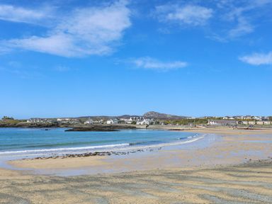 A sandy beach with calm blue sea and houses in the background at Min Y Mor Trearddur Bay in Trearddur Bay