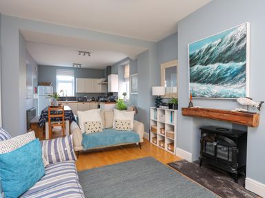 A living room with sofas a rug a fireplace a bookshelf and a kitchen with a dining table at Min Y Mor Trearddur Bay in Trearddur Bay