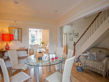 A dining room with a glass table and six white chairs next to a staircase and a wooden floor at Morfin in Criccieth