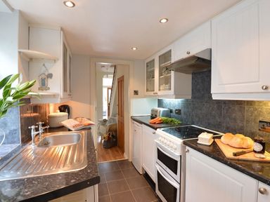A kitchen with a stainless steel sink white cabinets a stove with a toaster carrots and bread at Morfin in Criccieth
