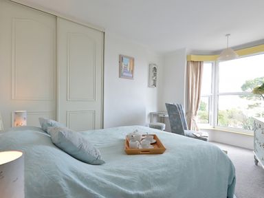 A bedroom with a bed and tea set on a tray by a window with curtains and an armchair at Morfin in Criccieth