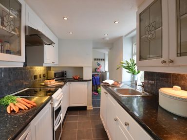 A kitchen with white cabinets black countertops carrots bread and a vase with leaves at Morfin in Criccieth