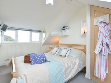 A bedroom with a double bed and pillows a wall-mounted television and a bathrobe hanging on the door at Morfin in Criccieth