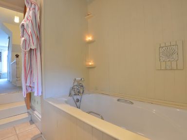 A bathroom with a bathtub candles on corner shelves and a robe hanging near the door at Morfin in Criccieth