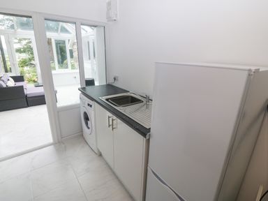 A utility room with a washing machine sink and fridge next to a glass door leading to a conservatory at Morfa Lodge in Porthmadog