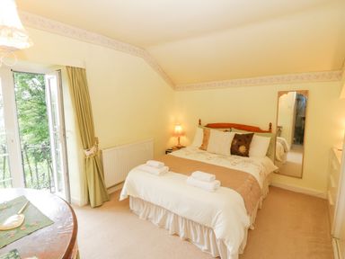 A bedroom with a double bed bedside lamps a mirror and glass doors with curtains at Morfa Lodge in Porthmadog