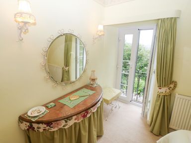 A dressing table with a round mirror and a stool by a window with green curtains at Morfa Lodge in Porthmadog