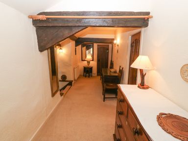 A narrow hallway with wooden beams a wooden dresser with a lamp a small table with two chairs and a mirror with a lamp on a side table at Morfa Lodge in Porthmadog