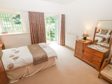 A bedroom with a single bed a wooden dresser with mirror a chair and curtains by a window at Morfa Lodge in Porthmadog