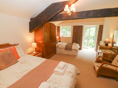 A bedroom with two beds a wooden wardrobe a bedside lamp a dressing table and an armchair at Morfa Lodge in Porthmadog