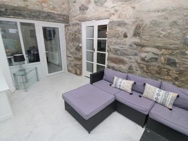 A room with stone walls a purple sofa with patterned cushions a glass table with a lamp and glass doors at Morfa Lodge in Porthmadog