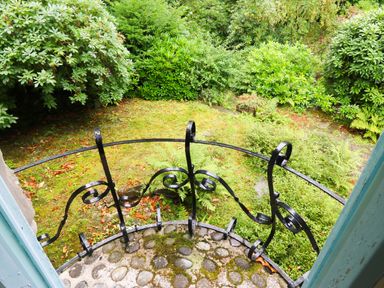 A small balcony with a black decorative railing overlooking a garden with green shrubs and mossy ground at Morfa Lodge in Porthmadog