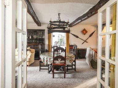 A dining room with a wooden table and chairs a cabinet and yellow curtains at Morfa Lodge in Porthmadog