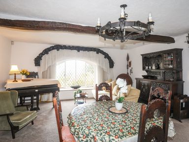 A dining area with a round table and carved wooden chairs a sofa near a large window and a wooden cabinet at Morfa Lodge in Porthmadog