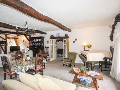 A living room with wooden beams dining table chairs piano and armchair at Morfa Lodge in Porthmadog