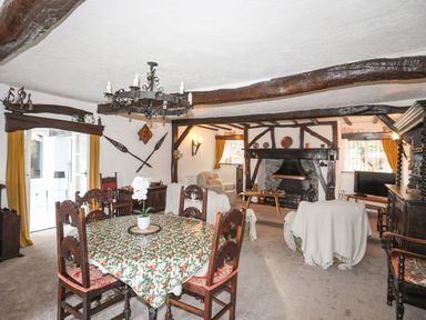 A dining and living area with wooden beams a round table with floral tablecloth and chairs and a fireplace at Morfa Lodge in Porthmadog