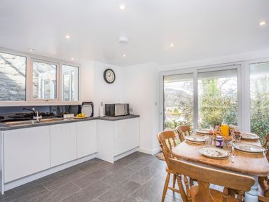 A kitchen with white cabinets a dining table set with plates and glasses and large windows at Morfa Lodge in Porthmadog