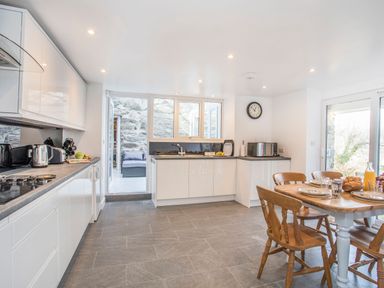A kitchen with white cabinets a wooden dining table with chairs and an outdoor seating area at Morfa Lodge in Porthmadog