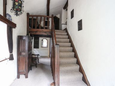 A hallway with carpeted stairs and wooden railing with antique furniture at Morfa Lodge in Porthmadog