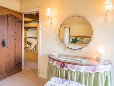 A bedroom with a wooden door a round mirror above a table with floral cloth and two wall lamps at Morfa Lodge in Porthmadog