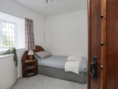 A small bedroom with a single bed bedside table lamp and a window with curtains at Morfa Lodge in Porthmadog