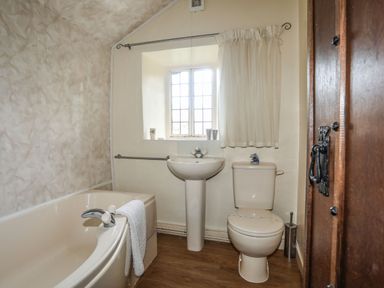 A bathroom with a bathtub a sink and a toilet under a window with a curtain at Morfa Lodge in Porthmadog