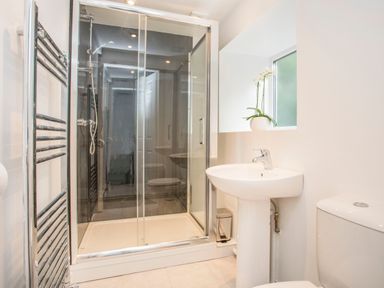 A bathroom with a shower enclosure a pedestal sink a toilet a window with a flower pot and a heated towel rail at Morfa Lodge in Porthmadog