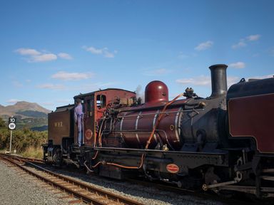 A steam locomotive train on railway tracks with a person standing on the side at Morfa Lodge in Porthmadog