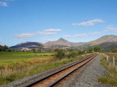 A railway track running through a grassy field with mountains in the background at Morfa Lodge in Porthmadog