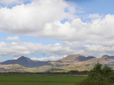 A mountain range with green fields and scattered trees under a cloudy sky at Morfa Lodge in Porthmadog