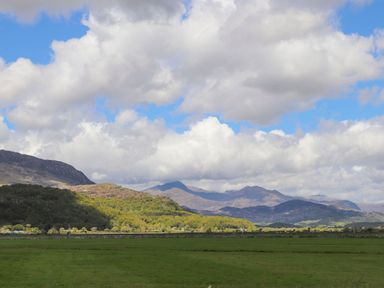 A green field with hills and mountains under a cloudy blue sky at Morfa Lodge in Porthmadog