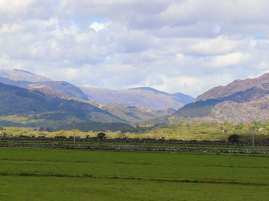Green grassy field with stone walls and mountains in the background under a cloudy sky at Morfa Lodge in Porthmadog