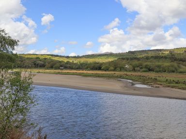 A river with a sandy shore and trees on hills under a cloudy sky at Morfa Lodge in Porthmadog
