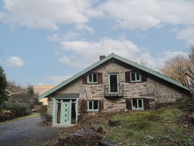 A stone house with green window frames and shutters surrounded by trees and grass at Morfa Lodge in Porthmadog