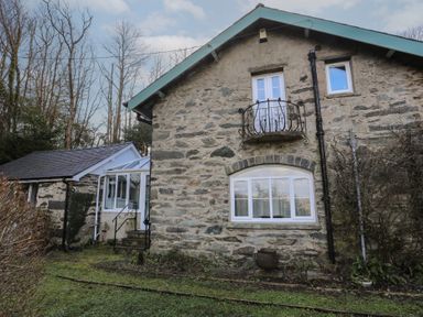 An exterior view of a stone house with white windows and a small balcony at Morfa Lodge in Porthmadog