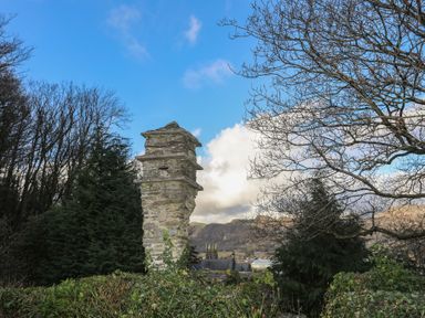 A stone pillar in a garden with trees and hills in the background at Morfa Lodge in Porthmadog