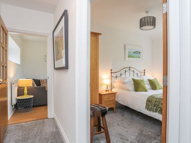 A hallway with a door to a bedroom with a bed and two green pillows and a door to a living room with a sofa and a lamp at Mynydd Parys in Brynsiencyn