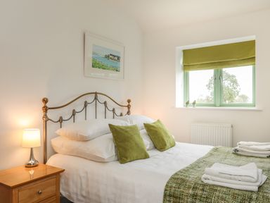 A bedroom with a metal bed frame a bedside table with a lamp and green cushions on the bed at Mynydd Parys in Brynsiencyn
