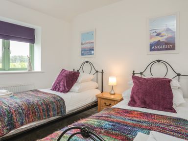 A bedroom with two single beds with colorful blankets and purple pillows at Mynydd Parys in Brynsiencyn