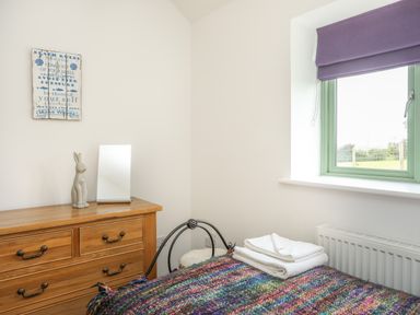A bedroom with a wooden dresser mirror and ceramic rabbit near a window with purple blinds at Mynydd Parys in Brynsiencyn
