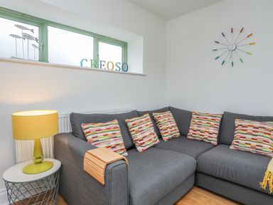 A gray sectional sofa with colorful patterned pillows a yellow table lamp and a clock on the wall at Mynydd Parys in Brynsiencyn
