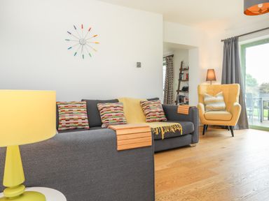 A living room with a gray sofa with colorful pillows a yellow armchair a yellow lamp and a clock on the wall at Mynydd Parys in Brynsiencyn