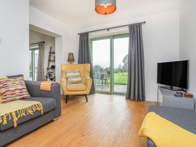 A living room with sofas pillows an armchair tv and sliding glass doors leading outside at Mynydd Parys in Brynsiencyn