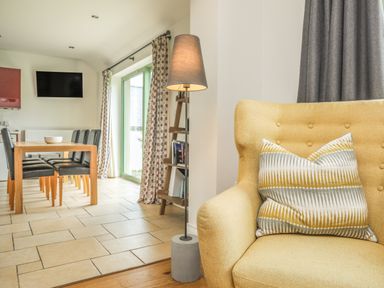 A yellow armchair with a patterned cushion near a floor lamp and a dining table with black chairs in a room with curtains at Mynydd Parys in Brynsiencyn